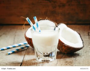 Coconut milk in a glass with striped straw and coconut halves, s